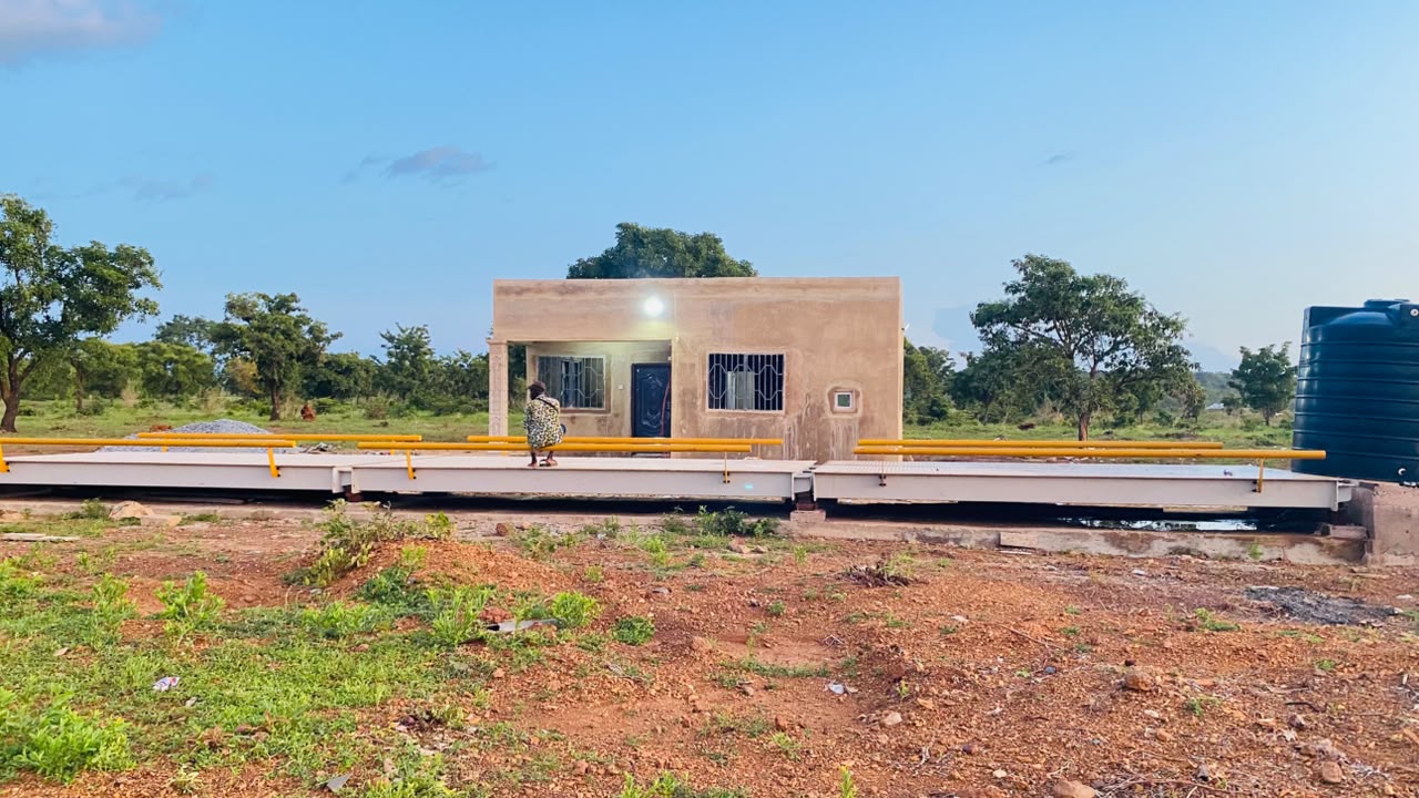 A three-section weighbridge platform with yellow guide rails and an operator office behind it, at the Hamile TradePoint.